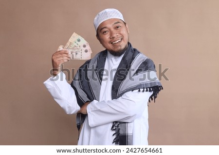 Asian Muslim man showing cash money banknotes over beige background