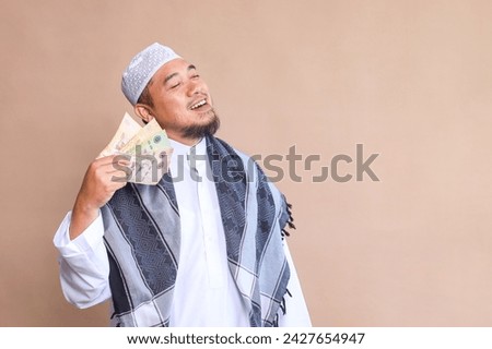Asian Muslim man showing cash money and looking aside over beige background