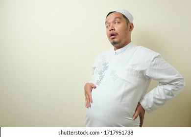 Asian Muslim Men Feel Very Full After Eating Too Much Food When Breaking The Fast. The Man Holds His Large Stomach Full Of Food