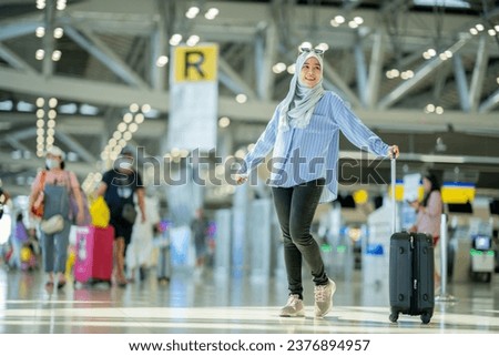 An Asian Muslim wearing a blue hijab is preparing for a vacation and she is at the international airport. She is waiting for her friends, Muslim travelers, holiday concept.