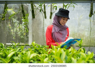 Asian Muslim woman farmer with clipboard recording plants in her greenhouse garden, flower farm, modern farming concept.  - Powered by Shutterstock