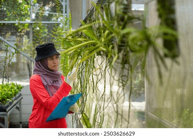 Asian Muslim woman farmer with clipboard recording plants in her greenhouse garden, flower farm, modern farming concept.  - Powered by Shutterstock