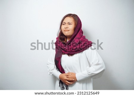 An Asian Muslim woman is fasting and hungry and touching her belly while looking aside thinking about what to eat
