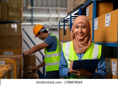 Asian Muslim Woman Holding Blue Color File Clamp For Record Goods Product. Two Warehouse Worker Work In Warehouse By Note And Scan Barcode.