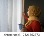 Asian Muslim Woman Holding A Cup And Staring Out Window While Open The Curtains At Home