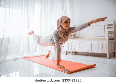 asian muslim woman instructor wearing hijab doing yoga pilates pose tutorial on orange mattress in a room - Powered by Shutterstock