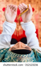Asian Muslim woman praying on carpet with beads chain wearing traditional dress