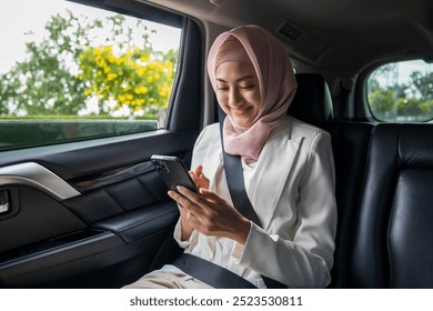 Asian muslim Woman Traveler sitting in car back seats using smartphone call taxi service in application and put on safety belt. Female islamic passenger in car traveling to destination. - Powered by Shutterstock