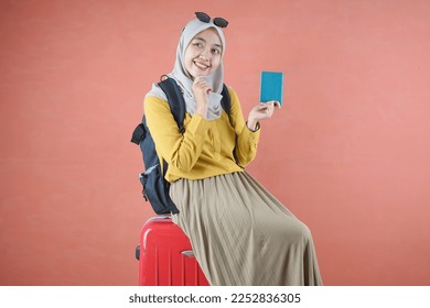 Asian Muslim woman traveling in a yellow t-shirt wearing a hijab, traveling with a luggage bag concept holding a passport. Isolated on brown background  - Powered by Shutterstock