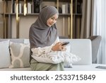 Asian muslim woman use smartphone at home, female in hijab checking messages, modern communication, smiling and holding mobile device technology use, staying connected, lifestyle concept, social media