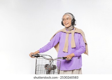 Asian Muslim woman is walking carrying a bicycle while smiling broadly turning her eyes to the right isolated - Powered by Shutterstock