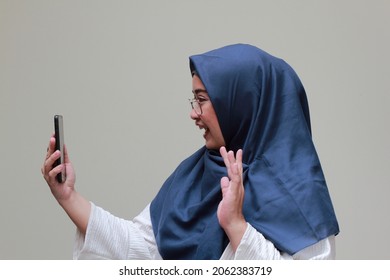 An Asian Muslim Woman Waving Her Hand While Having Video Call 