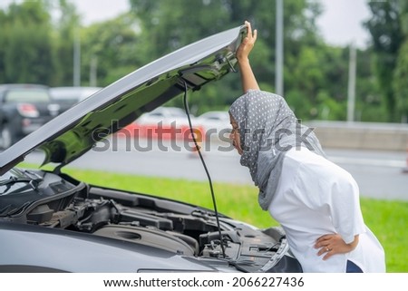 Asian Muslim women encountered a problem with the car driving the broken machine, opening the hood, checking the car, looking for the cause of the broken car.