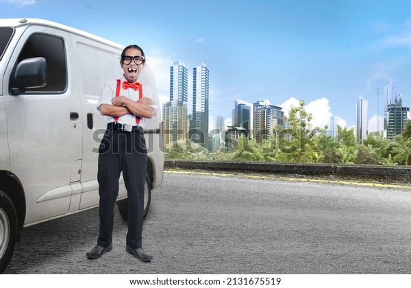 Asian nerd with ugly face standing\
beside the car on the street with cityscapes\
background