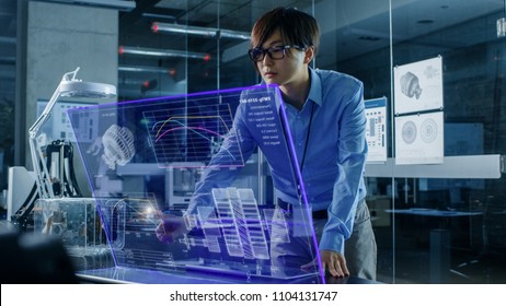 Asian Neural Microchip Design Engineer Uses Modern Computer With Transparent Holographic Display. Monitor Shows Advanced Technology Interface. Shot in Modern Glass and Concrete Office.