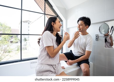 Asian new marriage couple brushing teeth together in bathroom at home. Attractive young man and woman feeling happy and relax, enjoy holiday honeymoon anniversary day then looking each other in house. - Powered by Shutterstock