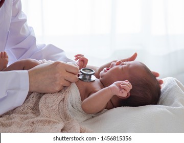 Asian newborn baby get sick crying during examine by pediatrician hold stethoscope, pediatric doctor monitoring heart pulse rate adorable infant crying in clinic, pediatrician with child concept