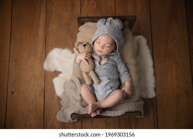 Asian Newborn Baby Weared Shirt With Hood Hugging Bear Doll On The Bed.