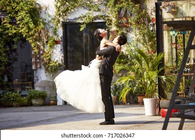 asian newly wed bride and groom celebrating marriage outside a building.