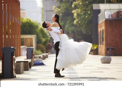 asian newly wed bride and groom celebrating marriage and hugging outside a building.