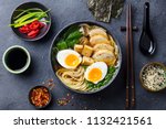 Asian noodle soup, ramen with chicken, tofu, vegetables and egg in black bowl. Slate background. Top view.