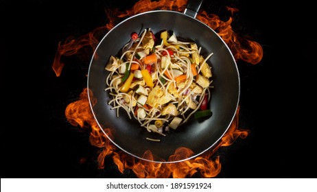 Asian Noodles In Wok Pan, Flames On Background. High Angle View Of Meat Preparation, Studio Shot.