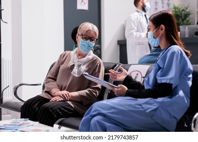 Asian Nurse Consulting Senior Woman In Waiting Room, Talking About Virus Prevention And Healthcare At Hospital Reception. Elderly Patient And Medical Assistant Chatting During Covid 19 Pandemic.