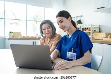 Asian Nurse At Nursing Home Take Care Of Disabled Senior Elderly Woman. Attractive Beautiful Therapist Doctor Use Laptop Computer And Show Diagnosis Treatment Plan To Older Grandma Patient In House.