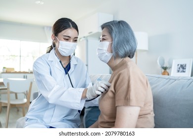 Asian nurse at nursing home take care of disabled senior elderly woman. Beautiful therapist doctor measure heart rate by stethoscope on female older patient on sofa. Medical insurance service concept.
