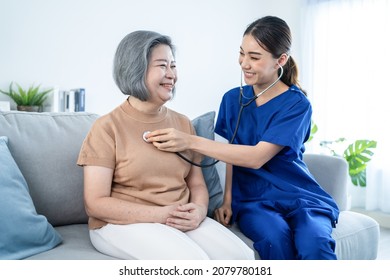 Asian Nurse At Nursing Home Take Care Of Disabled Senior Elderly Woman. Beautiful Therapist Doctor Measure Heart Rate By Stethoscope On Female Older Patient On Sofa. Medical Insurance Service Concept.