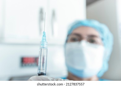 An Asian Nurse In Ppe Gear Checks A Syringe Filled With Drugs Prior To Injection. Selective Focus On The Needle. Hospital Or ER Scene.