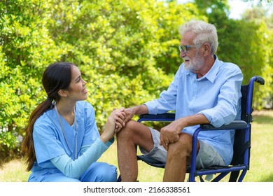 Asian Nurse Sitting On A Hospital Bed Next To An Older Man Helping Hands Care In Garden At Home. Elderly Patient Care And Health Lifestyle, Medical Concept.