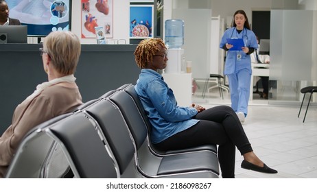 Asian Nurse Taking African American Woman To Do Checkup Visit With Doctor In Medical Office. Female Patient Waiting In Hospital Reception Lobby To Start Consultation Appointment.