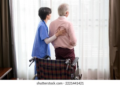 An Asian Nurse Taking Care Of An Elderly Man Getting Up From Wheelchair At Senior Healthcare Center.