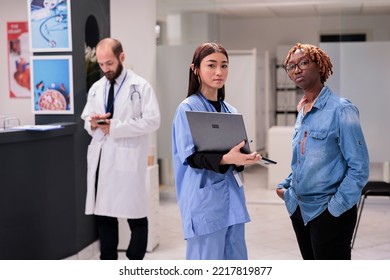 Asian Nurse, Young African American Woman Portrait At Hospital Waiting Room. Doctor Showing Patient Medication To Female Relative. Healthcare Professional Checking Program On Smartphone In Sanatorium.