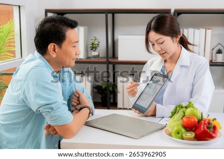 Asian nutritionist using tablet to explaining personalized meal plan with AI to patient during healthcare consultation, healthy lifestyle, woman dietitian showing nutrition plan with AI on tablet.