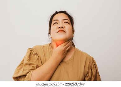 Asian obese woman having abnormal symptoms holding her neck with her hands because of pain feeling that there is a lump stuck in her throat which is a dangerous sign of oral cancer and lymphoma. - Shutterstock ID 2282637349