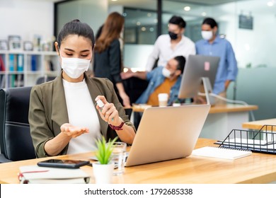 Asian office employee businesswoman wear protective face mask use alcohol spray hand sanitiser for hygiene in new normal office with social distance practice prevent coronavirus COVID-19 spreading.