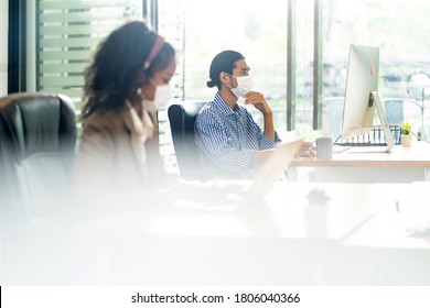 Asian Office employee with protective face mask working in new normal office with social distance practice to african colleague in foreground prevent coronavirus COVID-19 spreading. - Shutterstock ID 1806040366