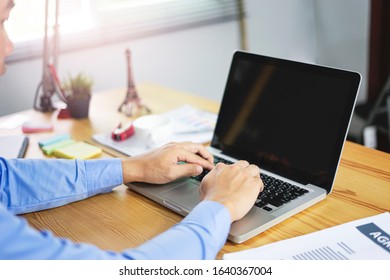asian office worker using and typing on his laptop computer, research and working hard on his business project, working on his wooden table within his office with documentations, calculator and pens 