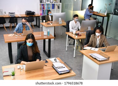 Asian Office Workers Wearing Face Masks Working In New Normal Office And Doing Social Distancing During Corona Virus Covid-19 Pandemic