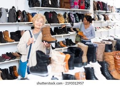 Asian And Old Caucasian Women Selecing New Shoes In Shop.