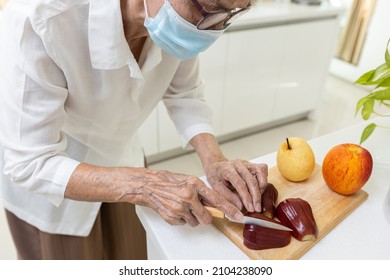 Asian Old Elderly People In A Medical Face Mask,cutting The Rose Apple Into Slices,senior Woman Eating Fresh Fruit Or Nutritious Food While Stay At Home,nutritional,healthy Food,health Care Concept