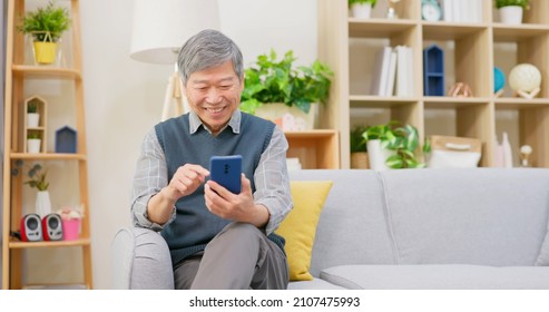 Asian Old Man Checks Social Media By Mobile Phone In Living Room At Home