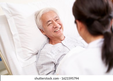 asian old man lying in bed talking to young female doctor in hospital ward - Powered by Shutterstock