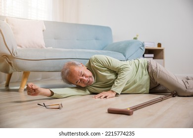 Asian Old Man Lying On Floor After Falling Down With Wooden Walking Stick, Sick Senior Man Beside Couch On Rug In Living Room At Home, Elderly Having An Accident After Doing Physical Therapy Alone