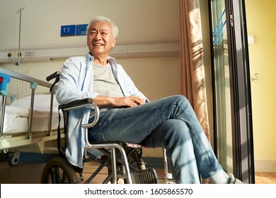 asian old man sitting in wheel chair in nursing home or hospital ward looking happy and content