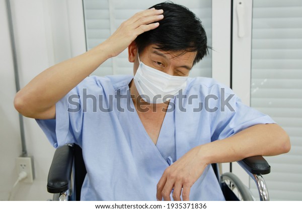 Asian\
Old man Wearing a mask to prevent disease and Covid 19 is sitting\
on wheelchair. He is Sick and headache for seriously ill in\
Hospital. Healthcare and Elderly society\
Concept