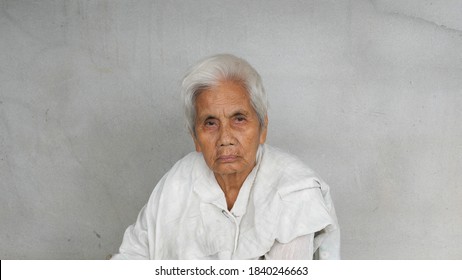 Asian Old Woman Looking To Camera With Serious Face Isolated Concrete Grey Wall Background. Rural Lifestyle Concept.