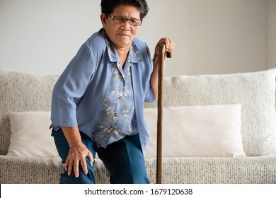 Asian Old Woman Sitting On Sofa And Having Knee Pain, Knee Injury At Home. Senior Healthcare Concept.